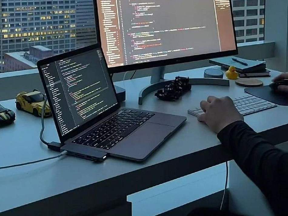 Developer coding on laptop and monitor with city view